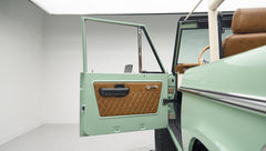 Classic Ford Bronco door open inside a white showroom with green exterior and tan interior upholstery