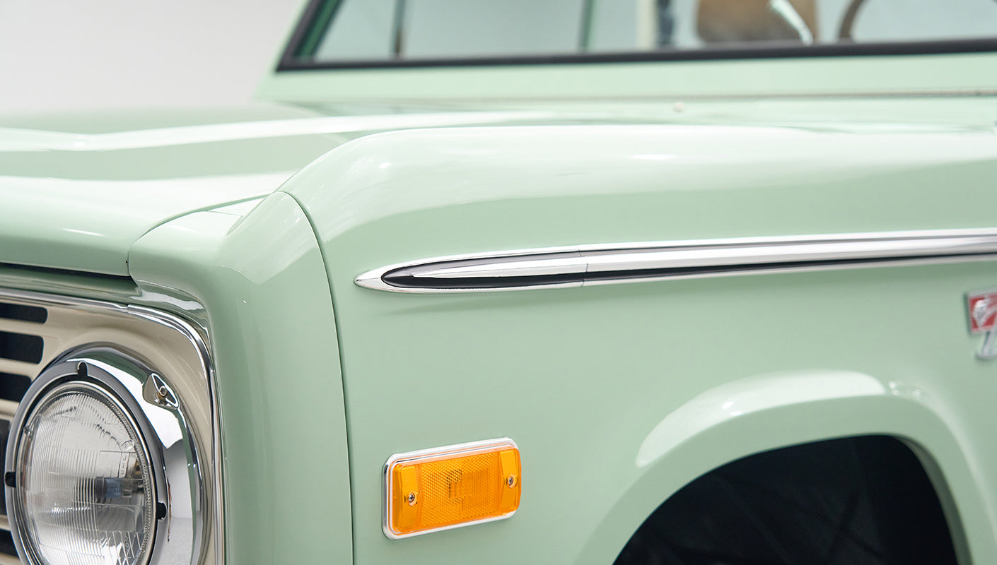 Close-up front of porcelain green Classic Ford Bronco showing headlight, grill, and chrome bumper