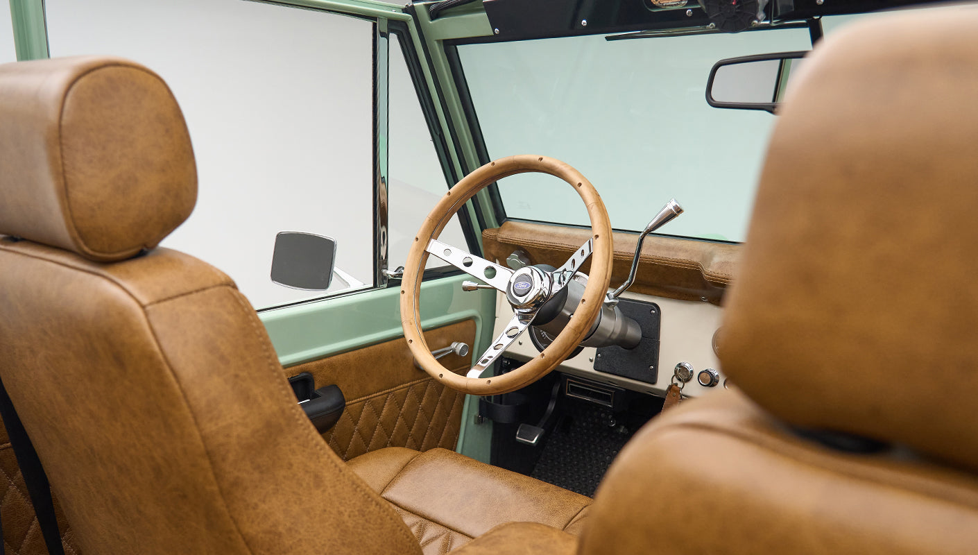 Front seats and steering wheel of Classic Ford Bronco with tan leather upholstery and green exterior