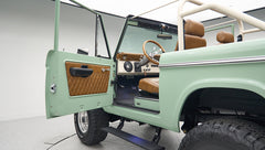 Classic Ford Bronco with open driver door showing green exterior and brown interior trim