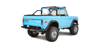 Blue Classic Ford Bronco rear view from passenger side, showing open top, tires, and tailgate with FORD lettering.