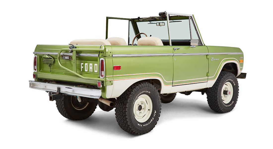Rear passenger angle of green Classic Ford Bronco with open roof and white seats