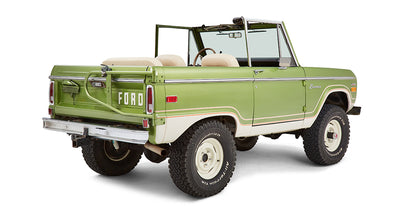 Rear passenger angle of green Classic Ford Bronco with open roof and white seats