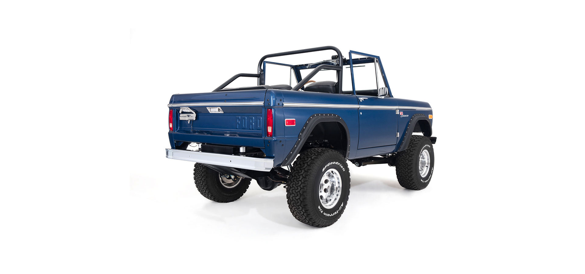 Rear three-quarter view of blue Classic Ford Bronco with roll cage, lifted tires, and chrome bumper on white background