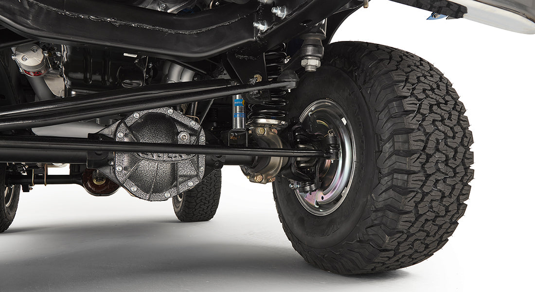 Underbody view of front suspension and axle with large off-road tires.