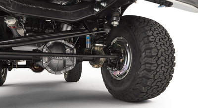 Underbody view of front suspension and axle with large off-road tires.