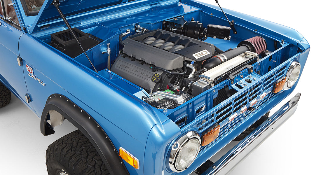 Close-up of V8 engine and front left fender area of sky blue Classic Ford Bronco.