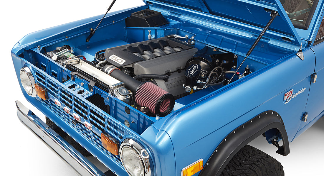 Open hood showing detailed engine bay of sky blue Classic Ford Bronco.