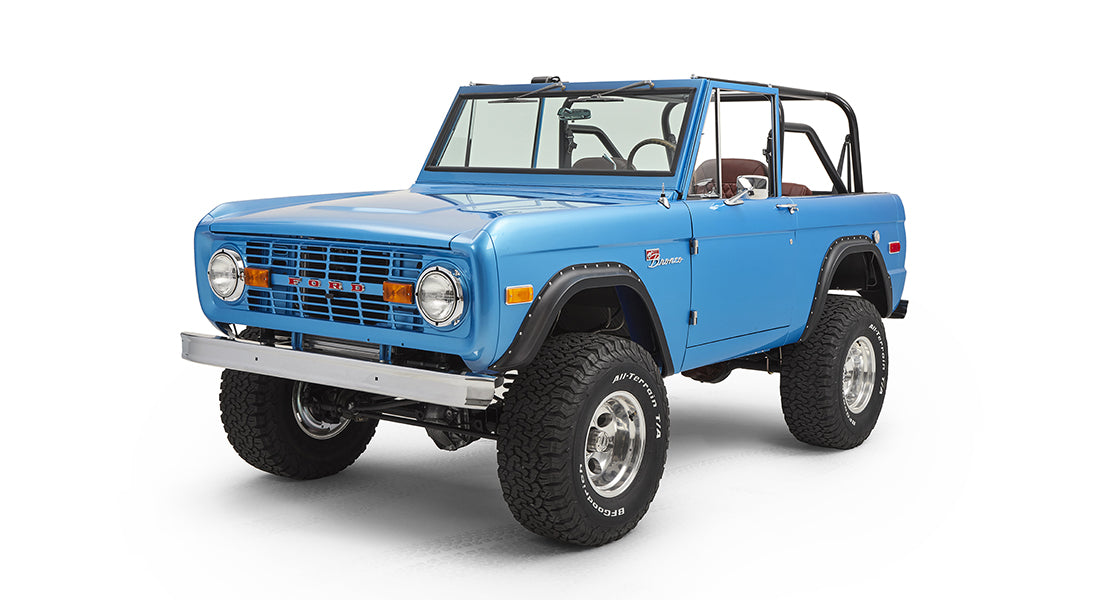 Front side view of sky blue Classic Ford Bronco showing grille, headlights, and large wheels.