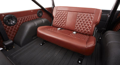 Interior rear area of Classic Ford Bronco featuring quilted brown leather bench seat and speakers