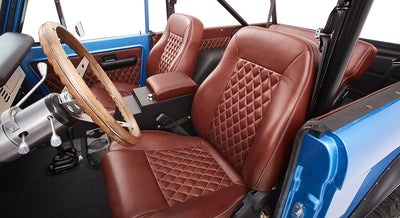 Front interior of Classic Ford Bronco showing quilted brown leather seats and wood steering wheel