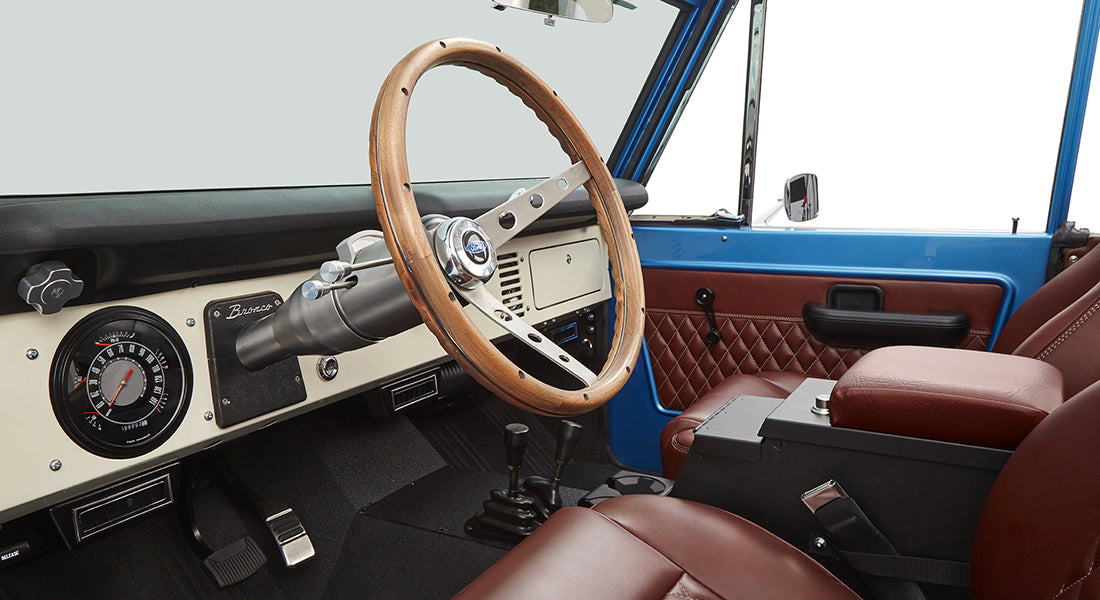 Interior of Classic Ford Bronco with wooden steering wheel and brown leather seats.