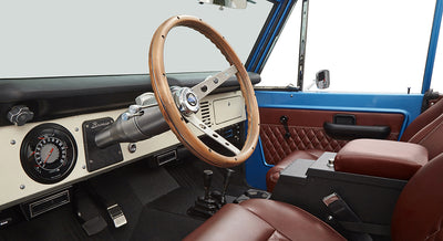 Interior of Classic Ford Bronco with wooden steering wheel and brown leather seats.