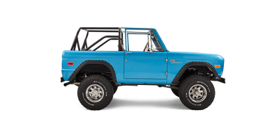 Side profile of sky blue Classic Ford Bronco with open roll cage and off-road tires on white background