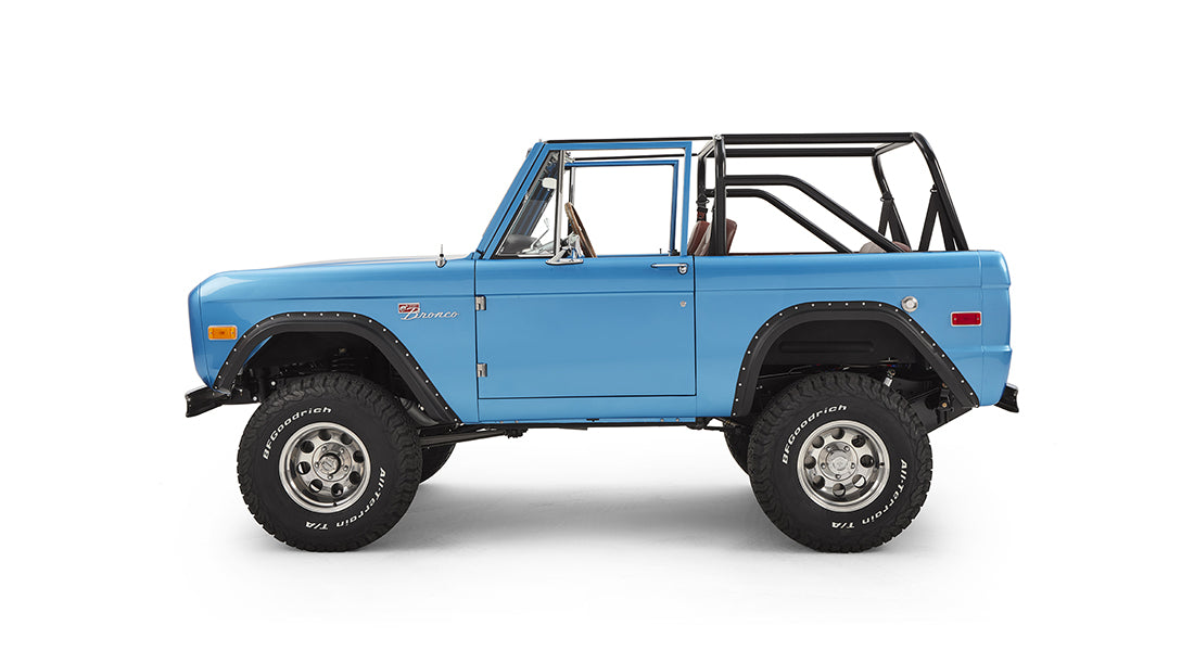 Side view of sky blue Classic Ford Bronco with roll cage and off-road tires on white background
