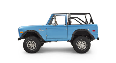 Side view of sky blue Classic Ford Bronco with roll cage and off-road tires on white background