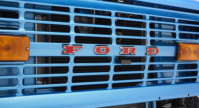 Front grille of sky blue Classic Ford Bronco with red FORD letters and amber lights