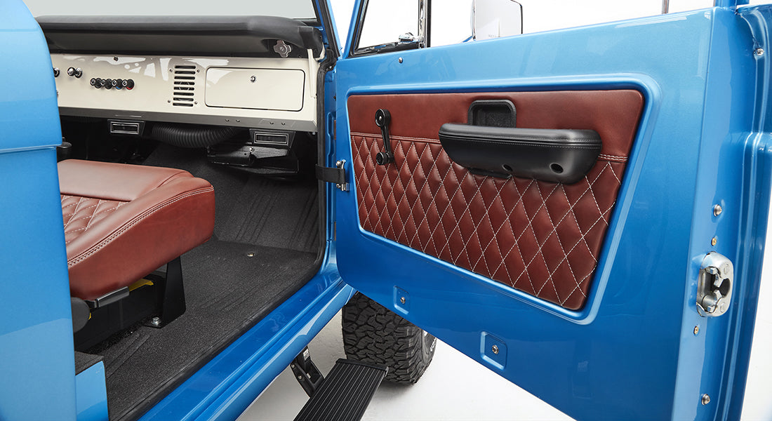 Open door showing brown diamond-stitched panel and part of driver's seat inside sky blue Classic Ford Bronco