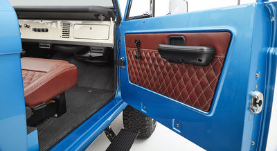 Open door showing brown diamond-stitched panel and part of driver's seat inside sky blue Classic Ford Bronco