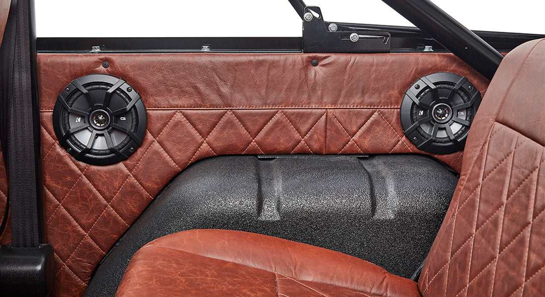 Two black round speakers mounted inside Classic Ford Bronco with brown leather interior