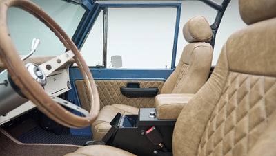 Interior view of Classic Ford Bronco focusing on tan seats, black steering column, and beige dashboard