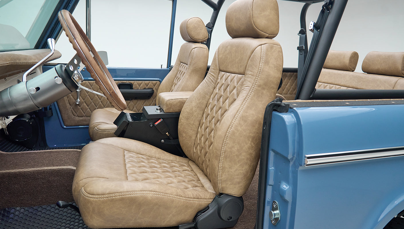 Open door showing front seats of Classic Ford Bronco with tan quilted upholstery and blue exterior