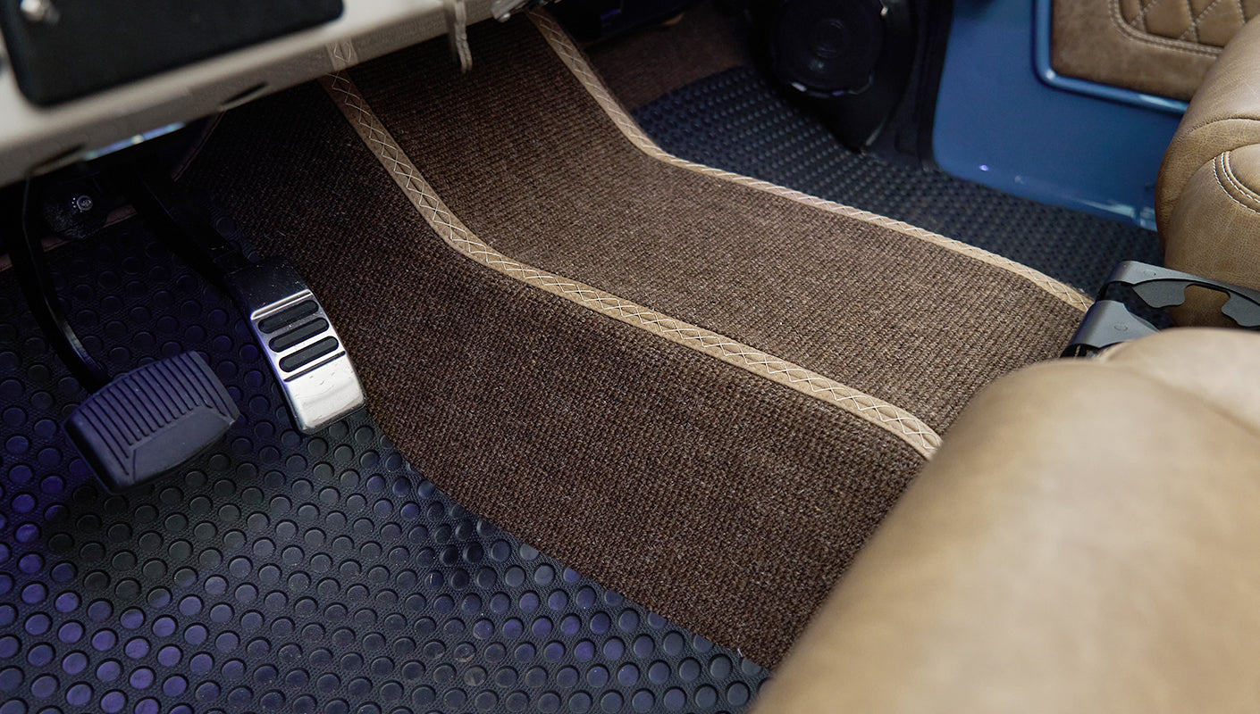 Floor area inside Classic Ford Bronco featuring brown carpet mat, pedals, and lower part of tan seats