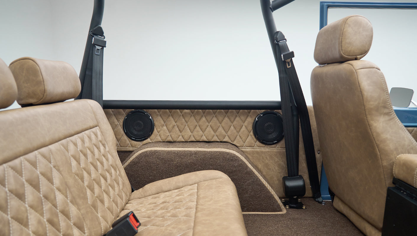 Rear seat area of Classic Ford Bronco with tan upholstery, brown carpeting, and roll bars visible
