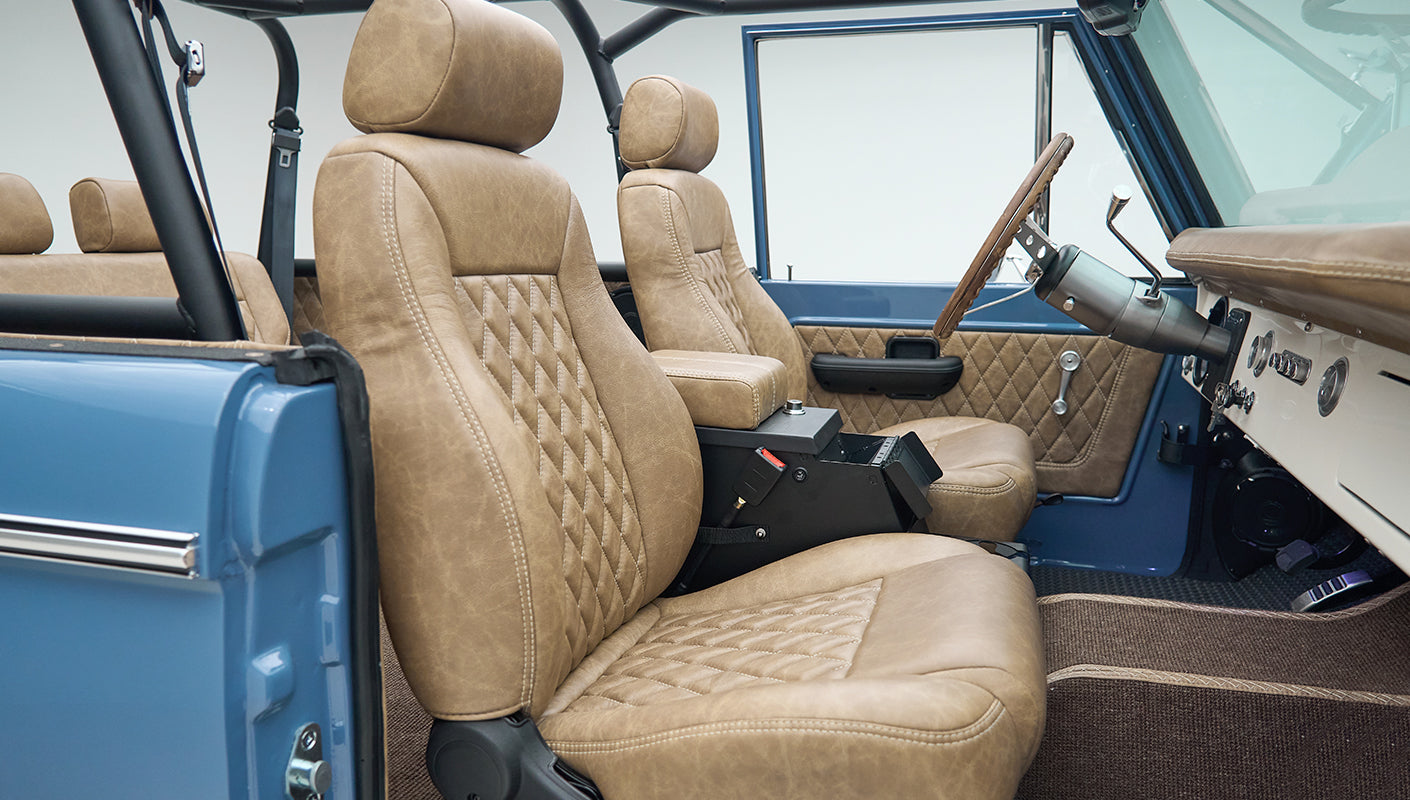 Side view of front seats inside Classic Ford Bronco with tan diamond-stitched upholstery and blue door frame