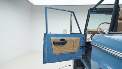 Open driver door showing diamond-stitched tan leather door panel on blue Classic Ford Bronco