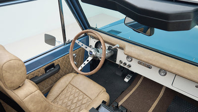 Driver cockpit view of Classic Ford Bronco showing steering wheel and quilted tan seats