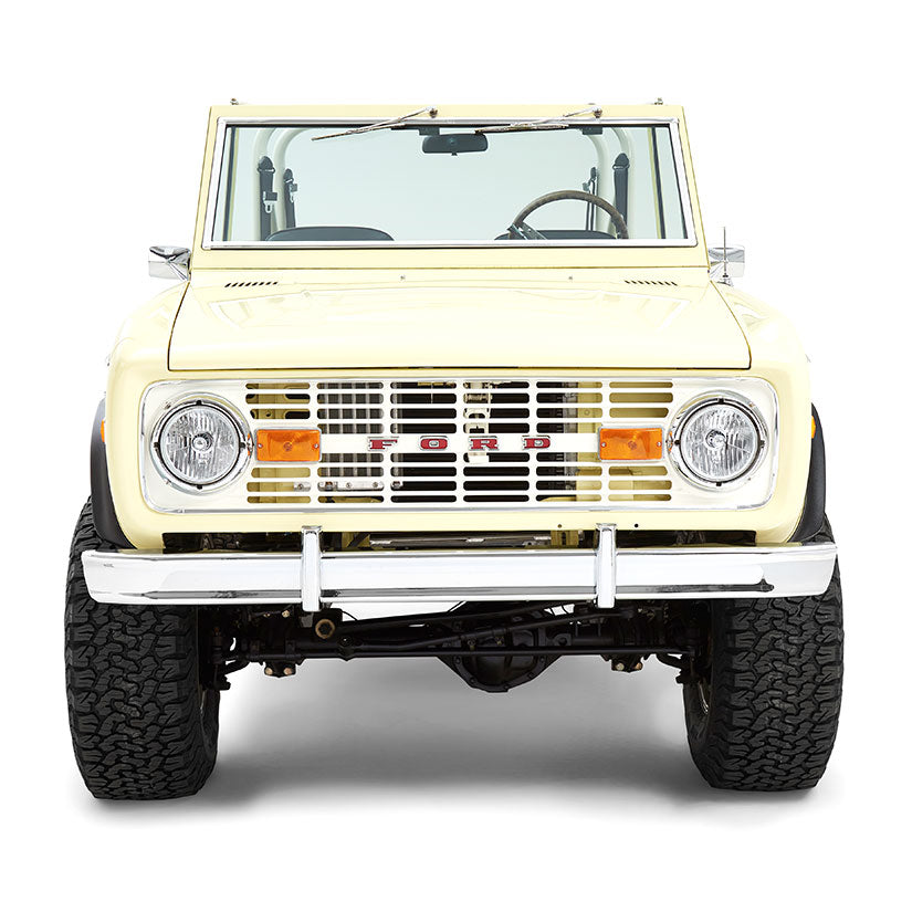 Front view of yellow Classic Ford Bronco featuring chrome bumper and round headlights on white background