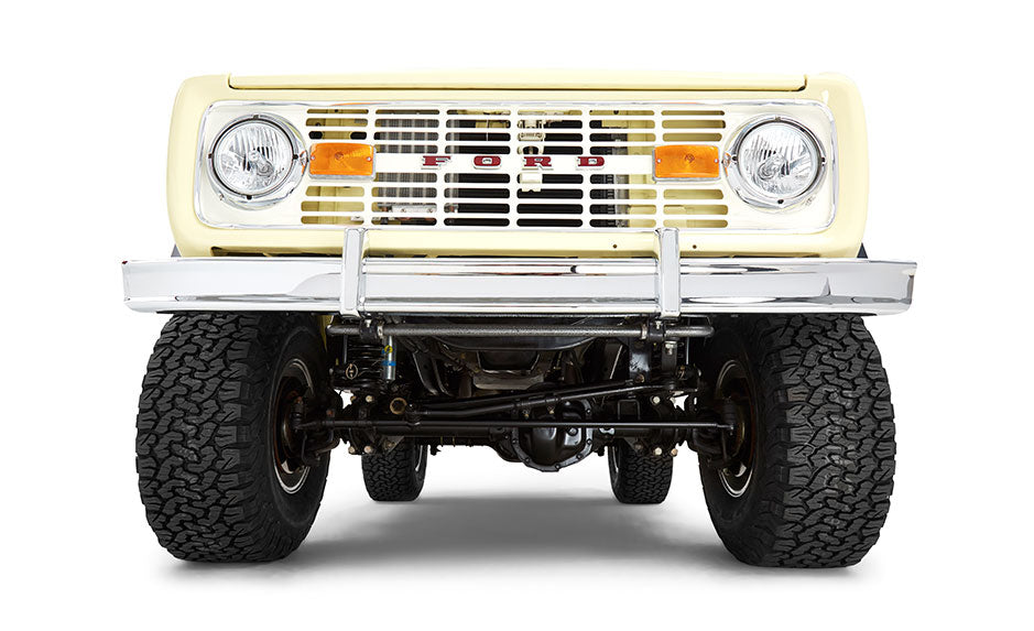 Front undercarriage view of yellow Classic Ford Bronco showing tires and suspension components on white background