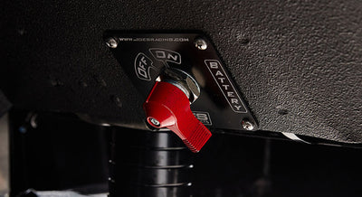 Red battery switch mounted under dashboard in Classic Ford Bronco with labeled metal plate