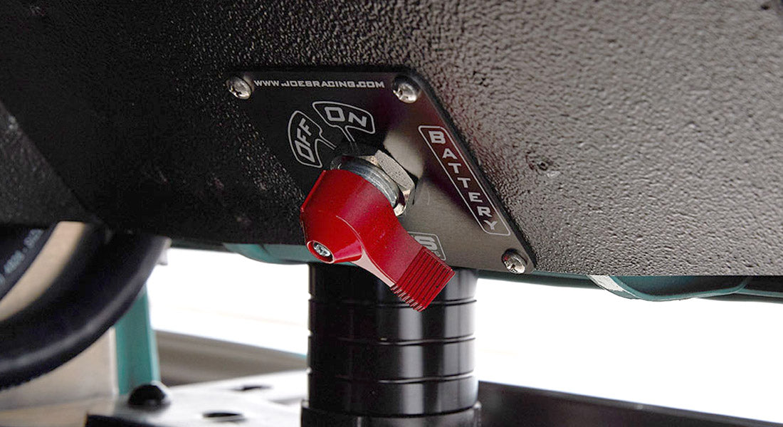 Red battery switch mounted under a vehicle with a black metal panel labeled on and off