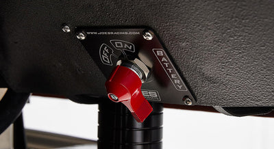 Red battery switch labeled "Off" and "On" mounted on a black textured surface with a metal plate.