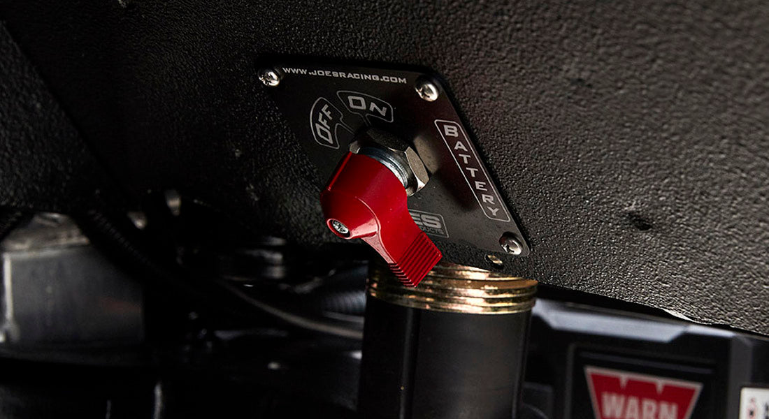 Close-up of red battery switch mounted under dashboard near wiring and warning label