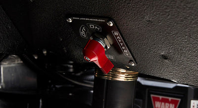 Close-up of red battery switch mounted under dashboard near wiring and warning label
