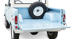 Rear bed of a light blue Classic Ford Bronco with tailgate open and spare tire inside