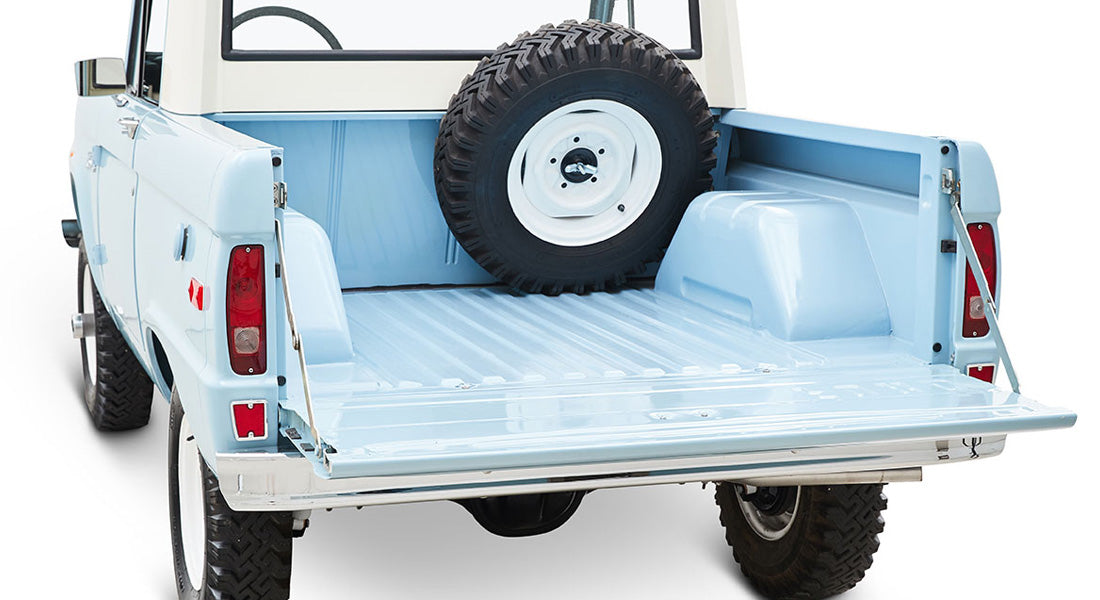 Rear bed of a light blue Classic Ford Bronco with tailgate open and spare tire inside