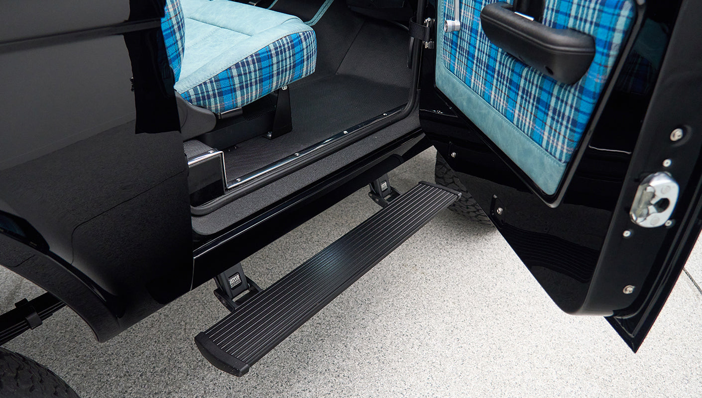 Side open door of Classic Ford Bronco showing black exterior and blue plaid interior seats