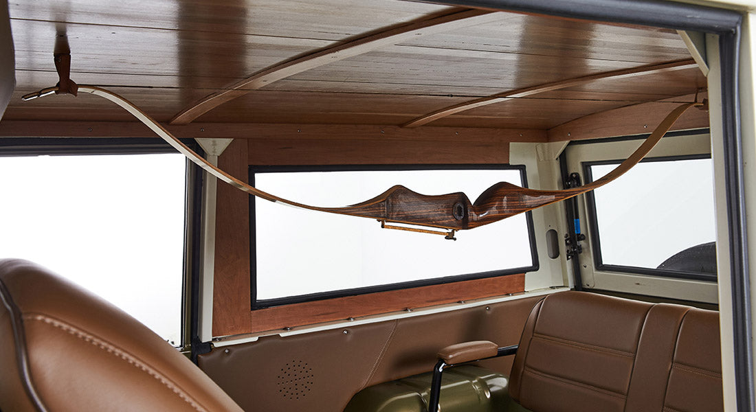 Wooden recurve bow hanging horizontally inside area with brown Classic Ford Bronco interior