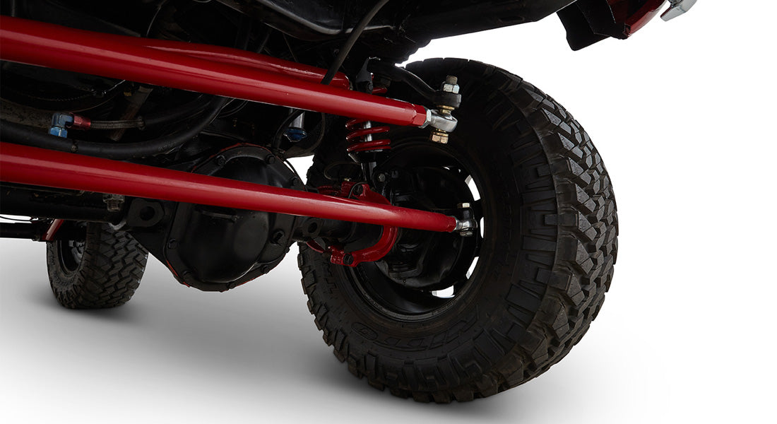 Close-up of front axle and suspension with red control arms and coil springs, mounted on off-road tire
