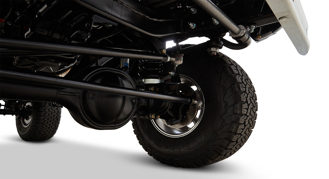 Detailed view of rear axle, suspension, and brake drum of a classic vehicle with off-road tires