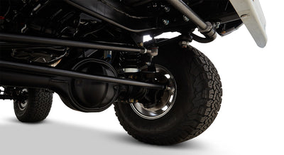 Detailed view of rear axle, suspension, and brake drum of a classic vehicle with off-road tires