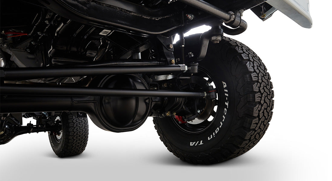 Undercarriage view showing a black axle and suspension parts with an all-terrain tire on a Classic Ford Bronco