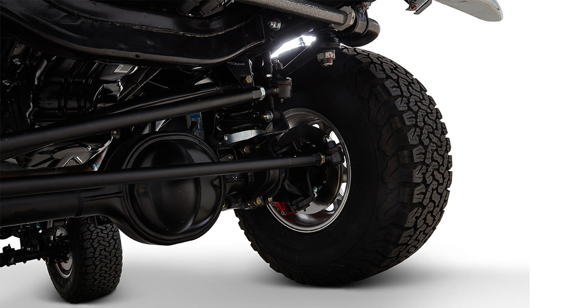 Suspension and axle close-up with rugged tire on Classic Ford Bronco against white background.