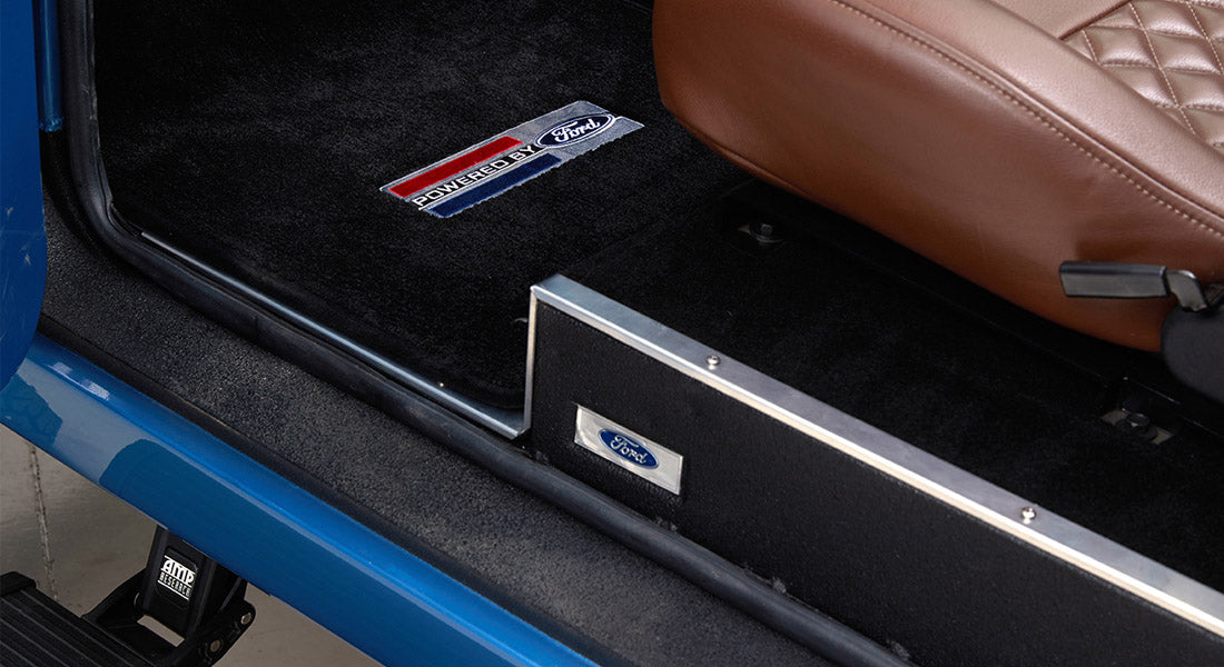 Interior floor area with black carpet and 'Powered by Ford' mat inside Classic Ford Bronco.