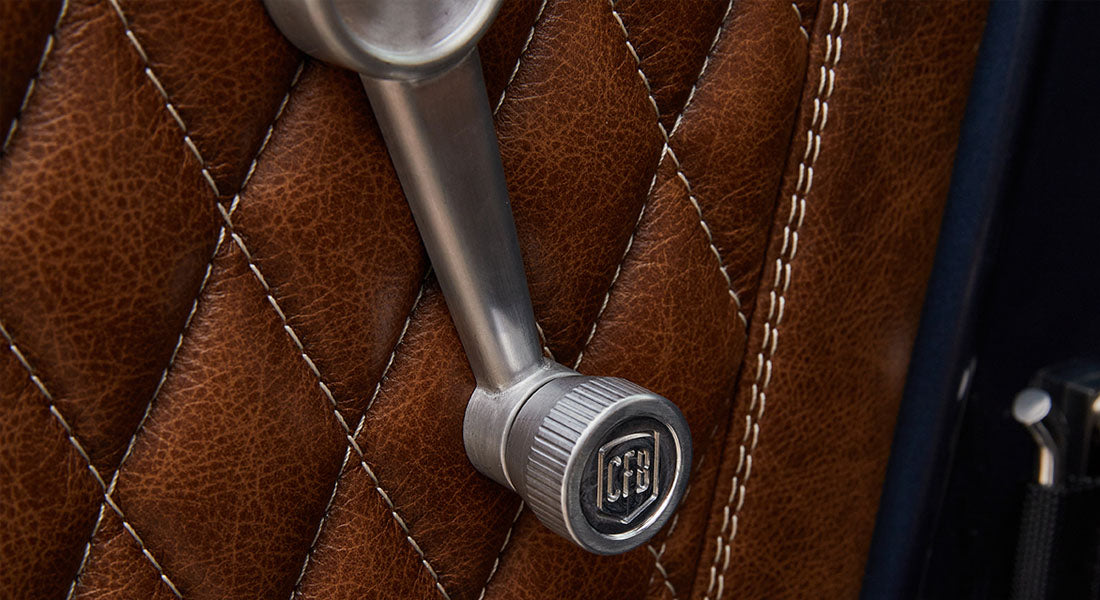 Close-up of metal window crank handle over brown diamond-stitched leather