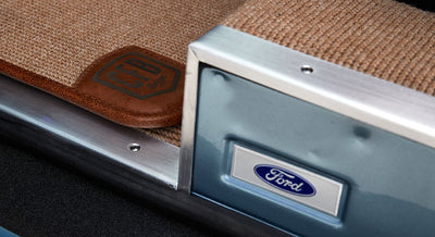 Metal door sill plate with blue Ford emblem above beige carpet and brown leather inside Classic Ford Bronco
